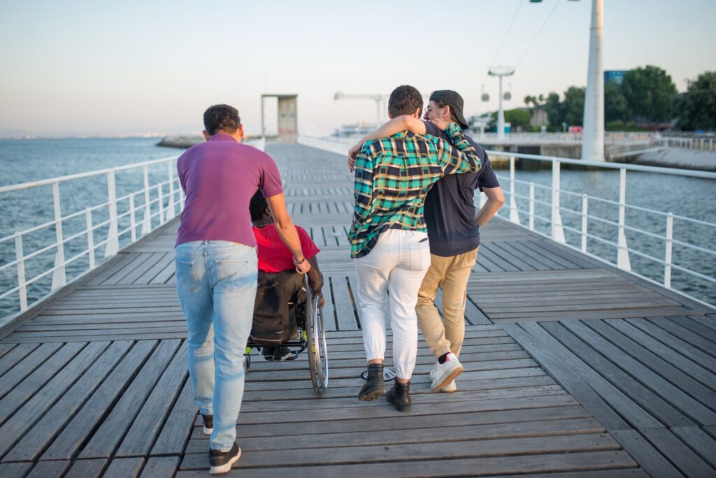 Group of friends walking along a scenic boardwalk by the sea, promoting friendship and accessibility.