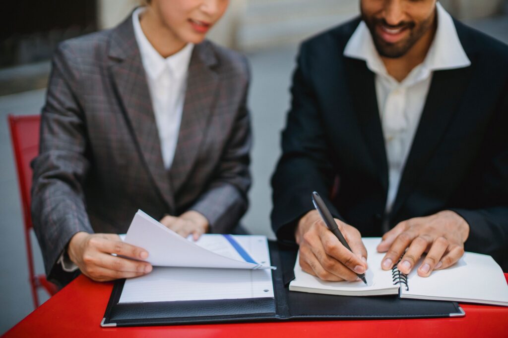 Two business professionals in suits reviewing documents and writing notes at a table.